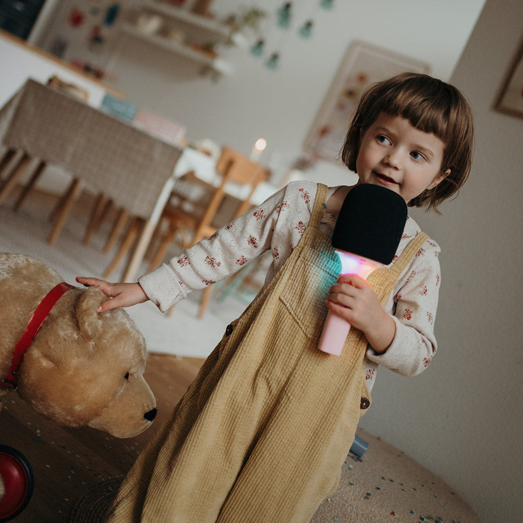 Child holding a microphone and teddy bear in a room with decorations