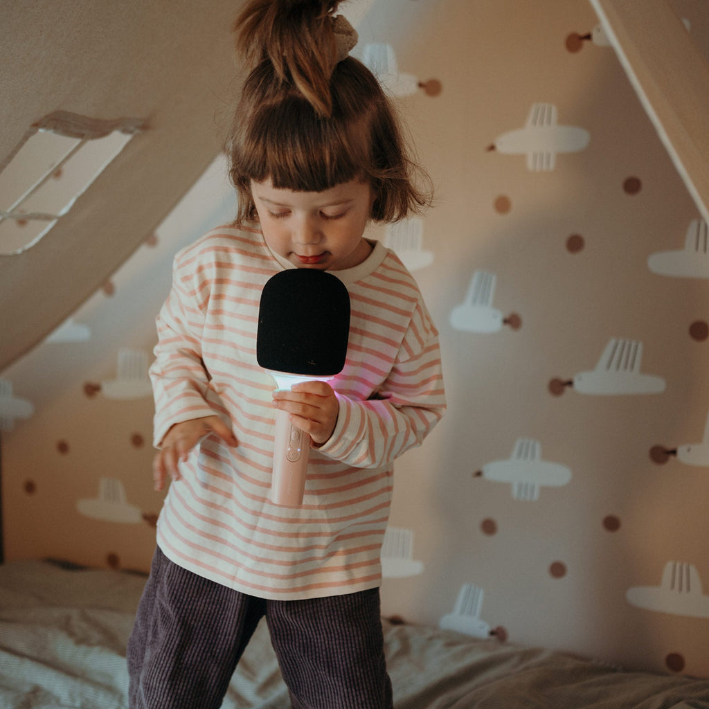 Child holding a microphone in a room with airplane patterned wallpaper