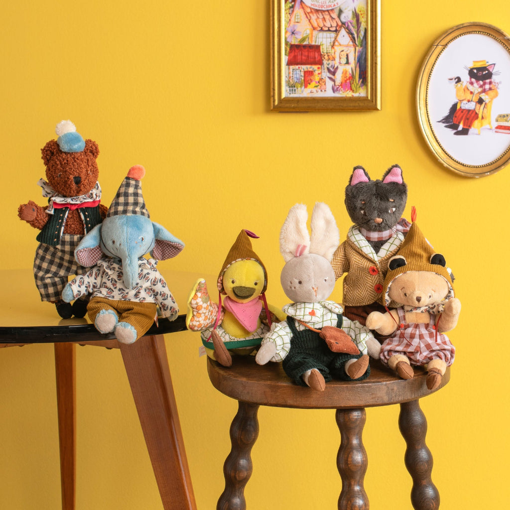 Collection of stuffed animals on a wooden table against a yellow wall with framed pictures.