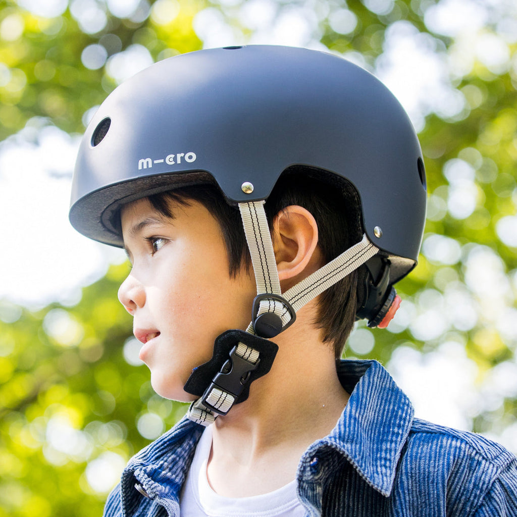 Boy in a denim jacket wearing a dark Micro helmet with grey straps, side profile outdoors