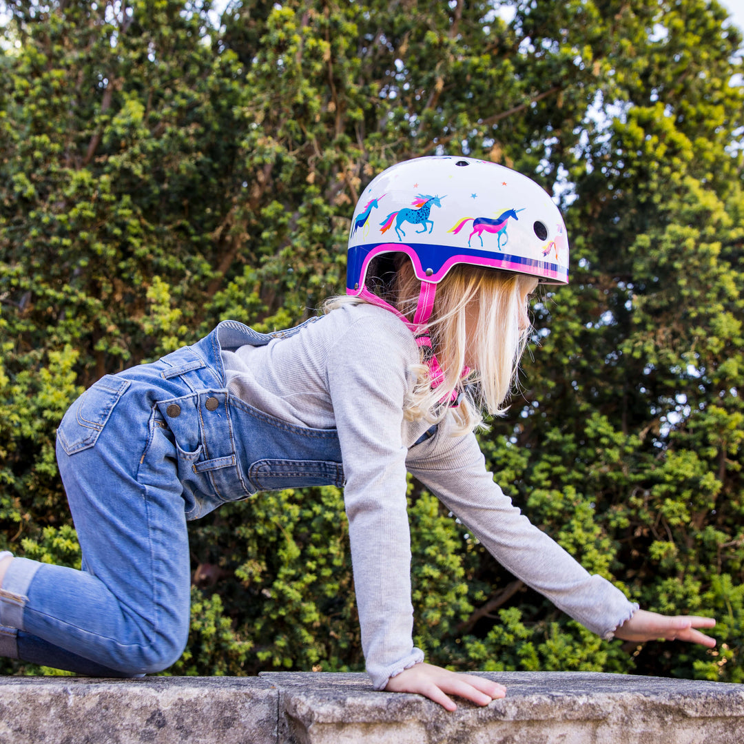 Girl in denim dungarees wearing the Unicorn Micro helmet, climbing on a low stone wall