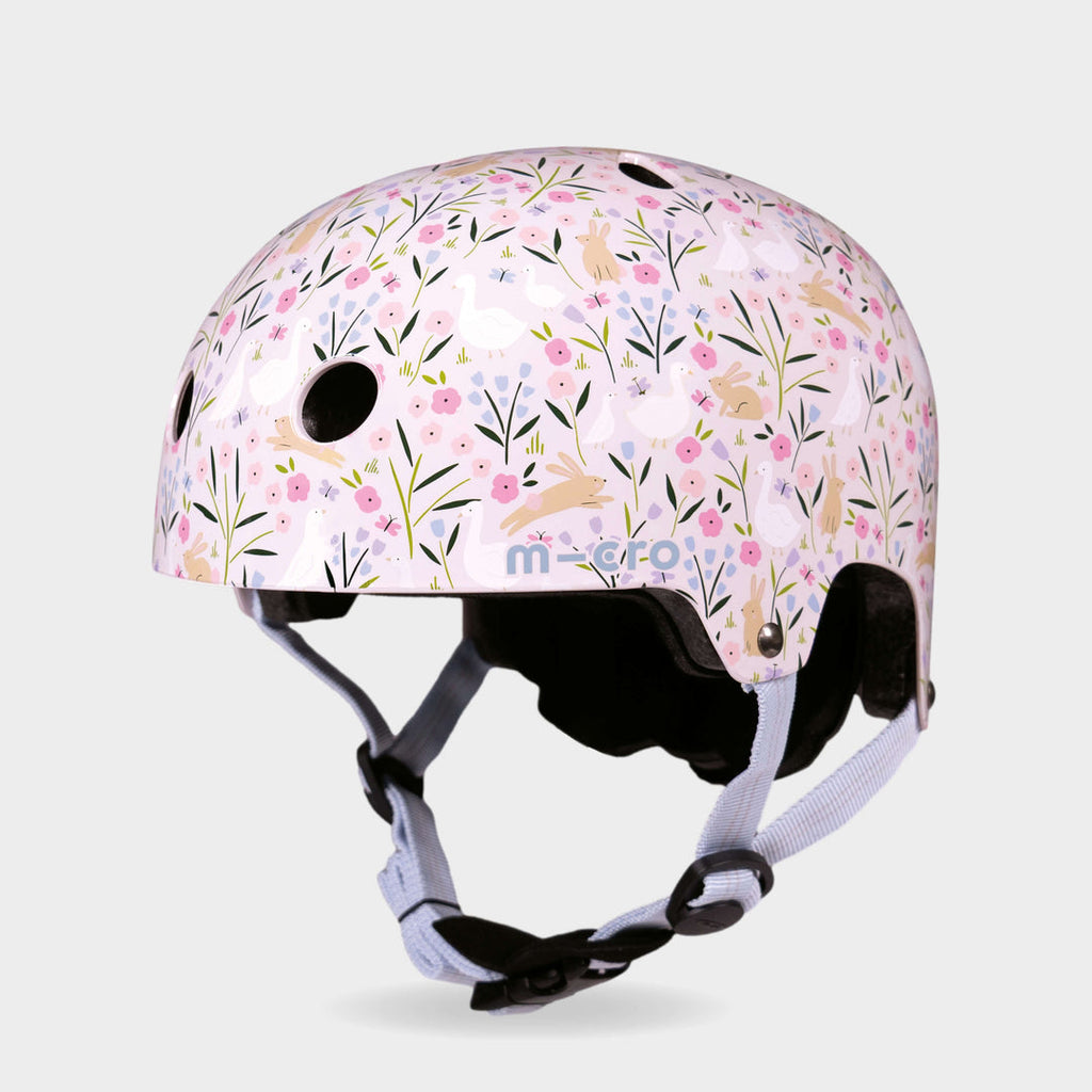 Micro printed helmet in pale pink with a flower and leaping hare pattern and lilac straps, front three-quarter view