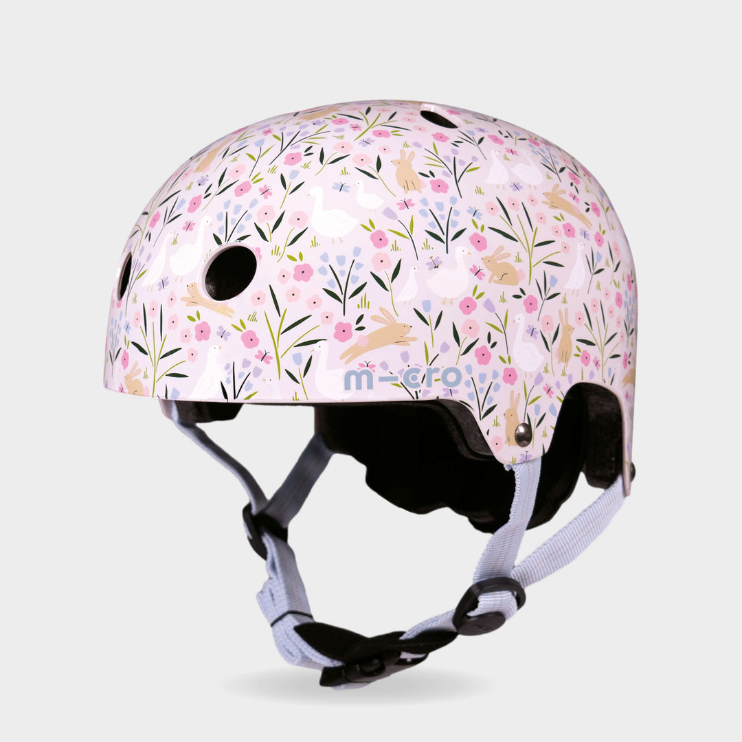 Micro printed helmet in pale pink with a flower and leaping hare pattern and lilac straps, front three-quarter view