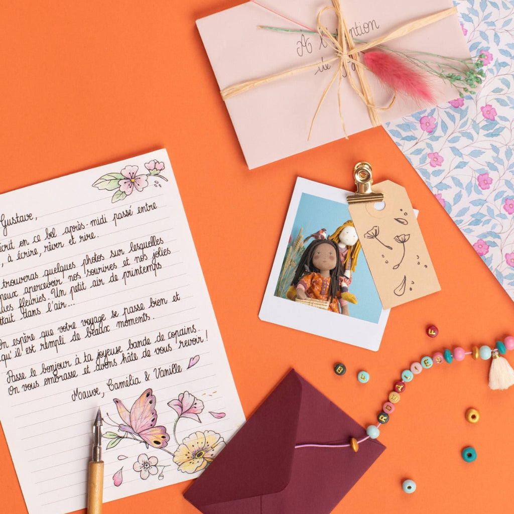 Flat lay of stationery items including a letter, envelope, photo, and decorative elements on an orange background.