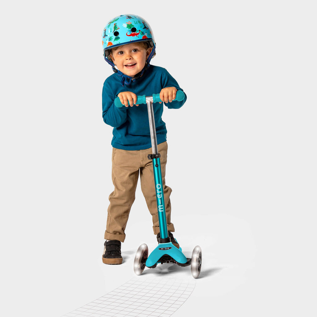 Smiling boy in a helmet and blue jumper riding the aqua Mini Micro Deluxe LED scooter