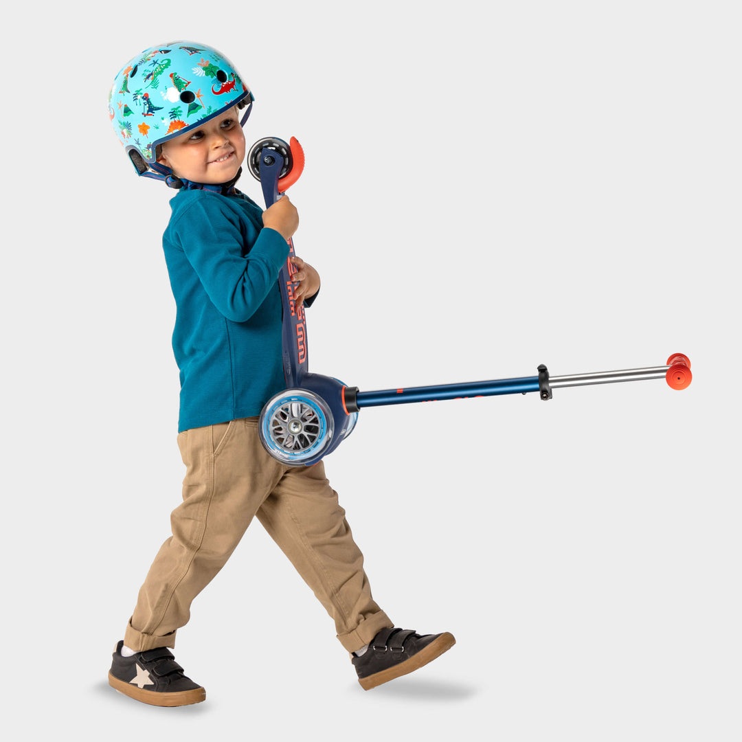Boy in a helmet walking and pulling the navy Mini Micro Deluxe scooter by its handlebar