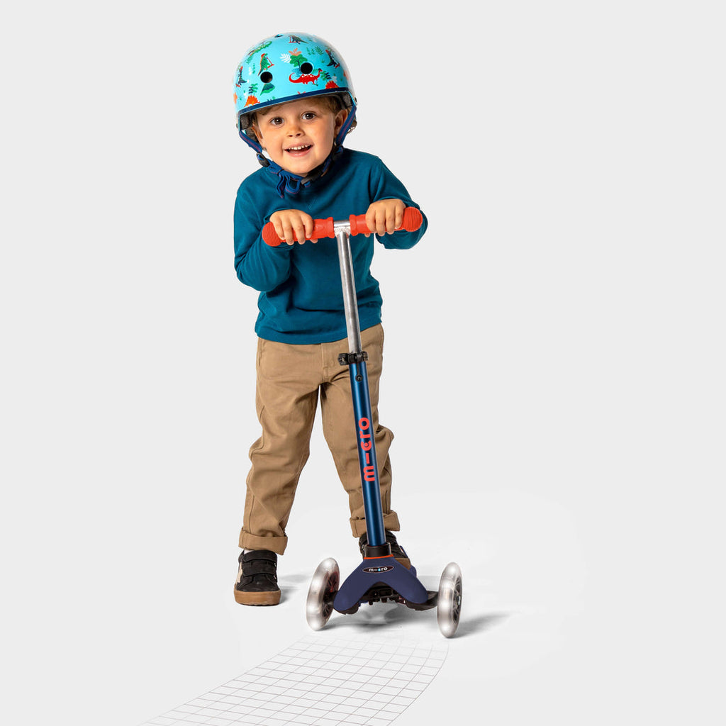 Smiling boy in a helmet and blue jumper riding the navy Mini Micro Deluxe LED scooter