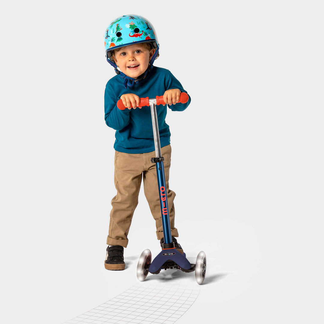 Smiling boy in a helmet and blue jumper riding the navy Mini Micro Deluxe LED scooter