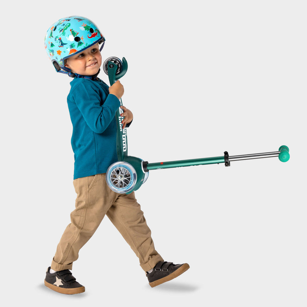 Boy in a helmet walking and pulling the green Mini Micro Eco scooter by its handlebar