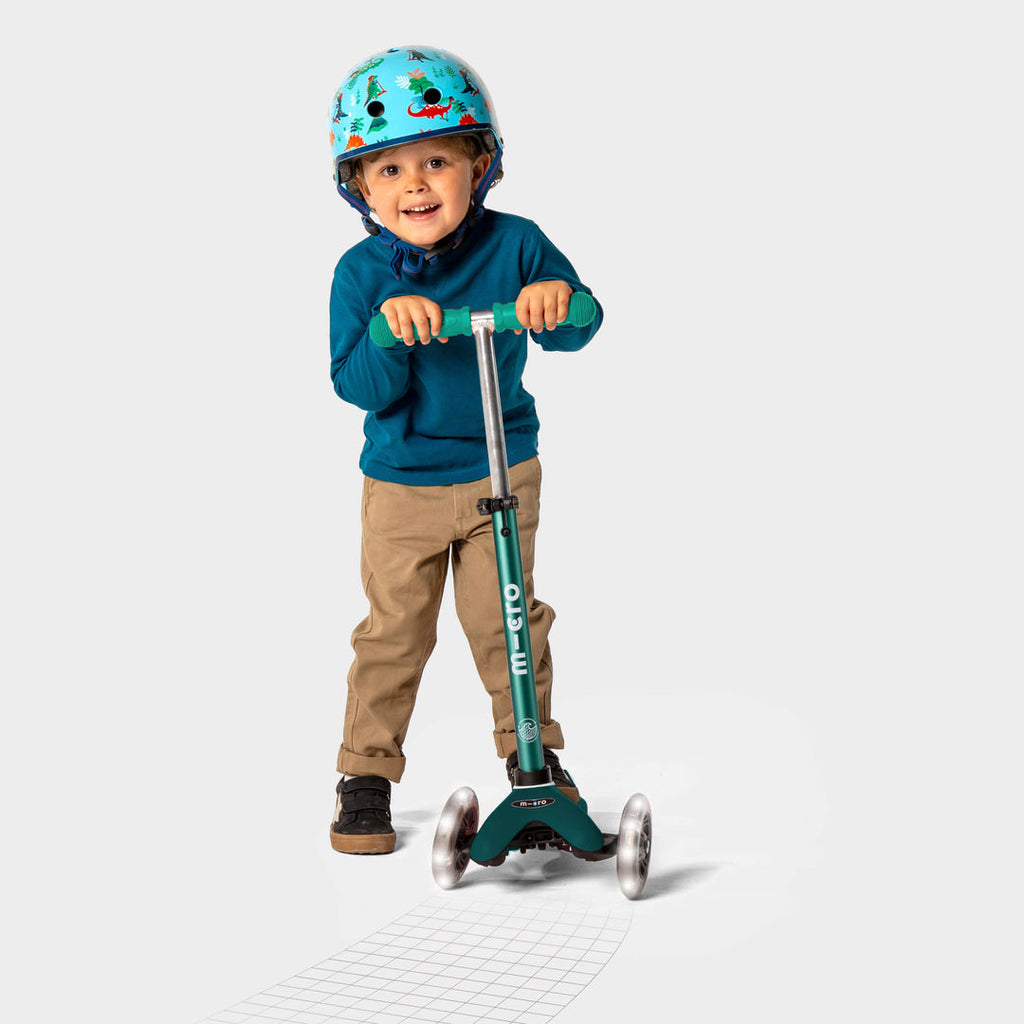 Smiling boy in a helmet and blue jumper riding the green Mini Micro Eco LED scooter