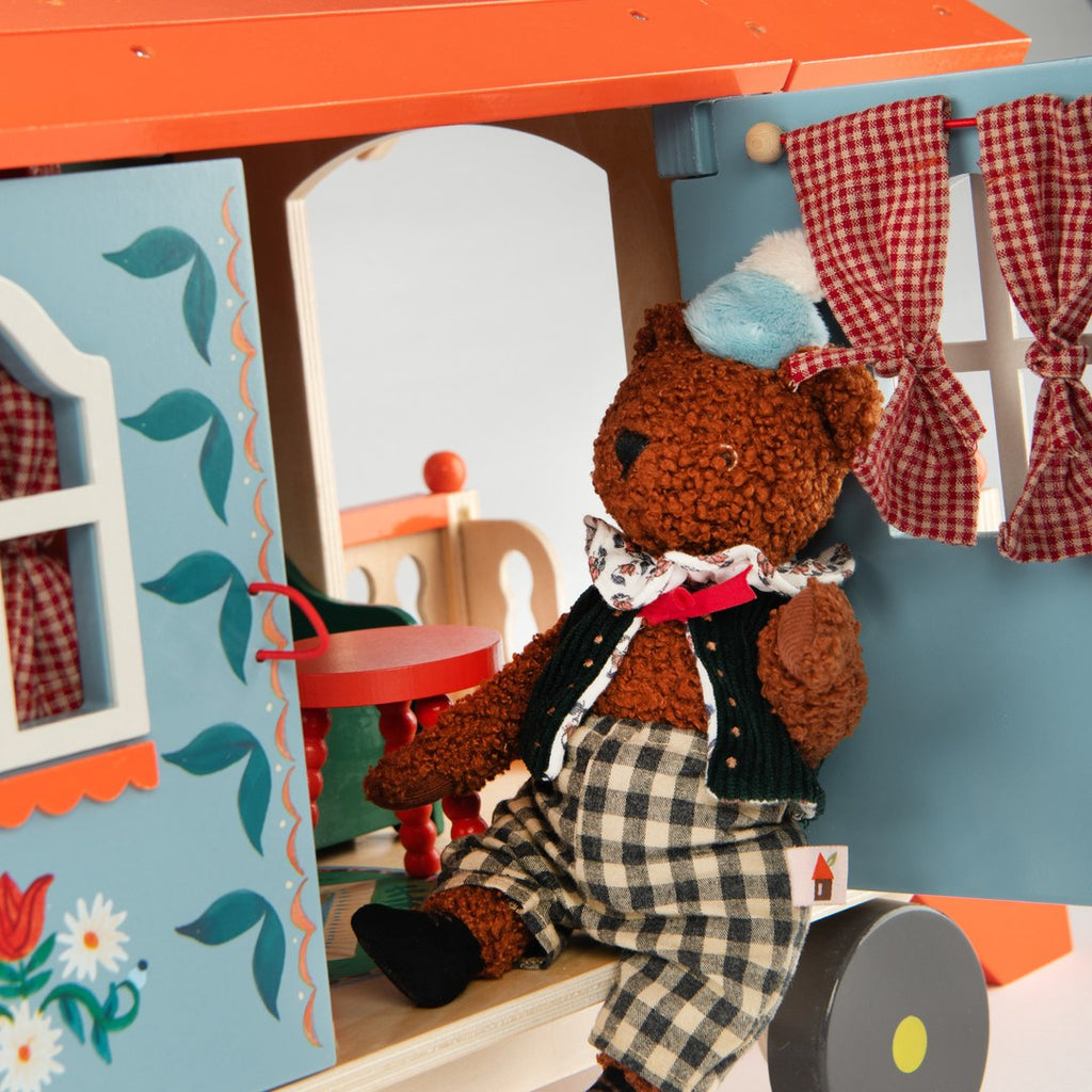 Bear doll sitting on the doorstep of the Moulin Roty wooden caravan