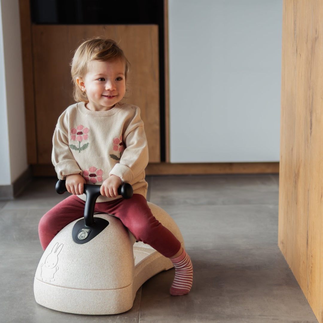 Child sitting on a cream my first scoot and ride.