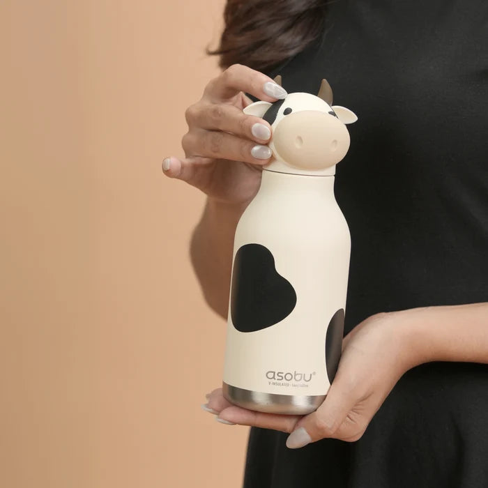 Person holding a cow-shaped water bottle with a heart design on a beige background
