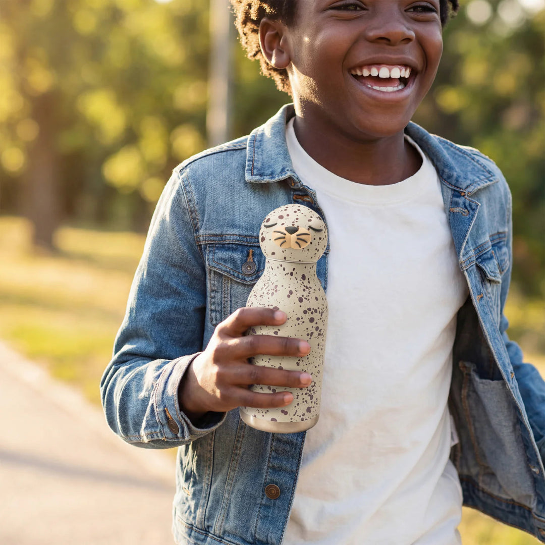 Child holding a seal character water bottle outdoors with greenery in the background