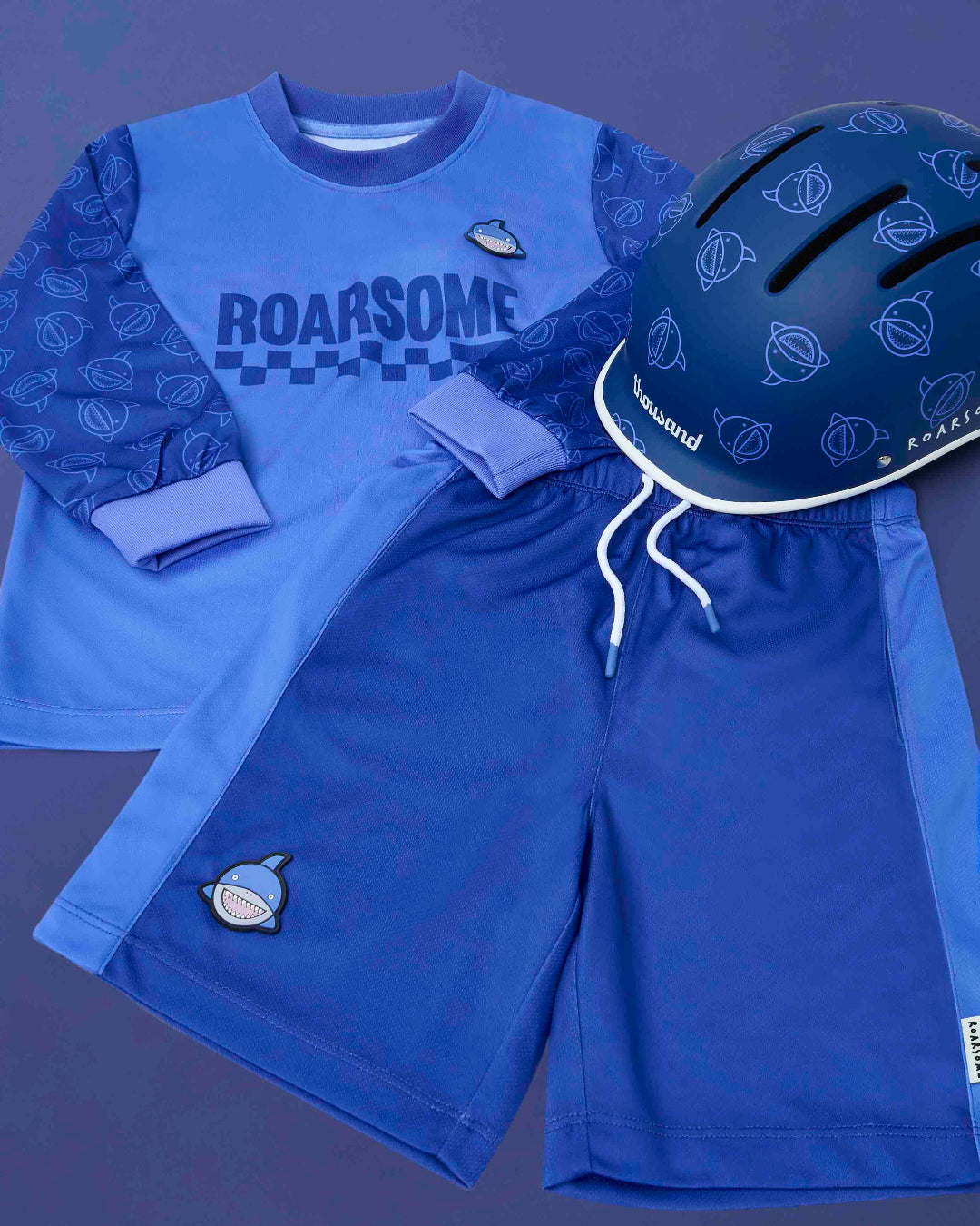 Blue children's outfit with 'ROARSOME' text, helmet, and shorts on a dark background