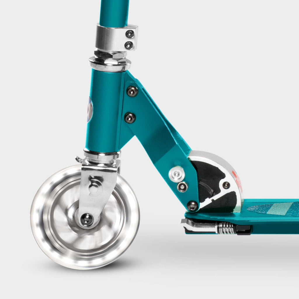 Close-up of the light-up LED front wheel and folding mechanism on the aqua Micro Sprite scooter
