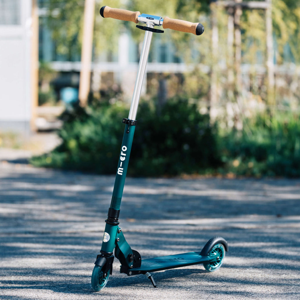 Green Micro Recycled Sprite LED scooter standing on a sunlit path in a park