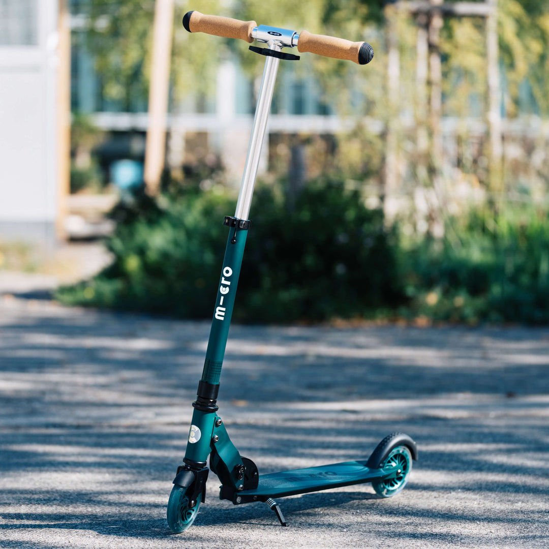 Green Micro Recycled Sprite LED scooter standing on a sunlit path in a park