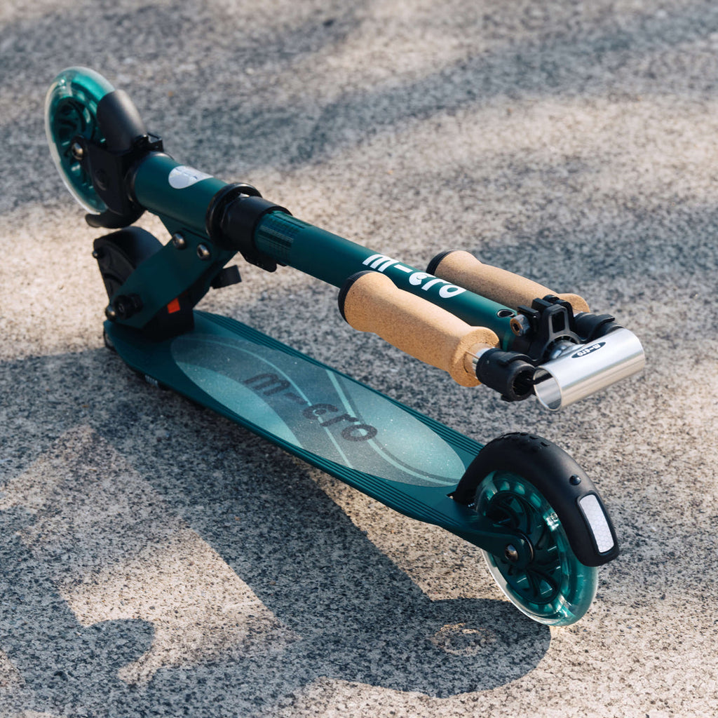 Folded green Micro Recycled Sprite scooter lying on gravel with its cork grips