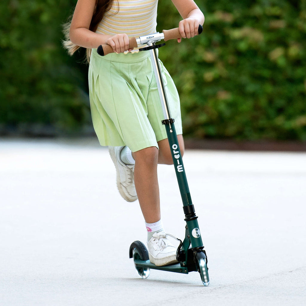 Girl in a green skirt riding the green Micro Recycled Sprite LED scooter