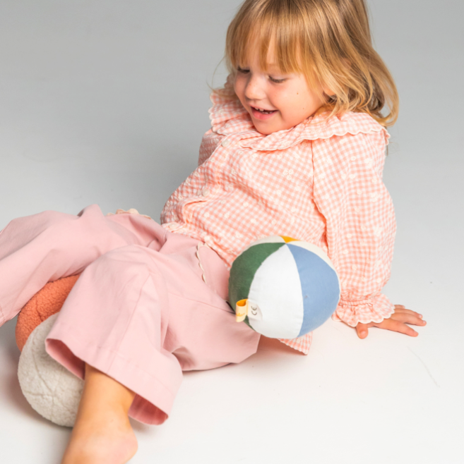 Child playing with a colourful ball toy on a plain background