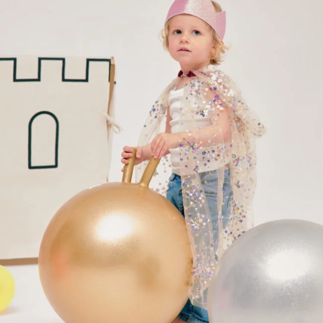 Child holding a gold space hopper jump ball with a white wall and decorative elements in the background