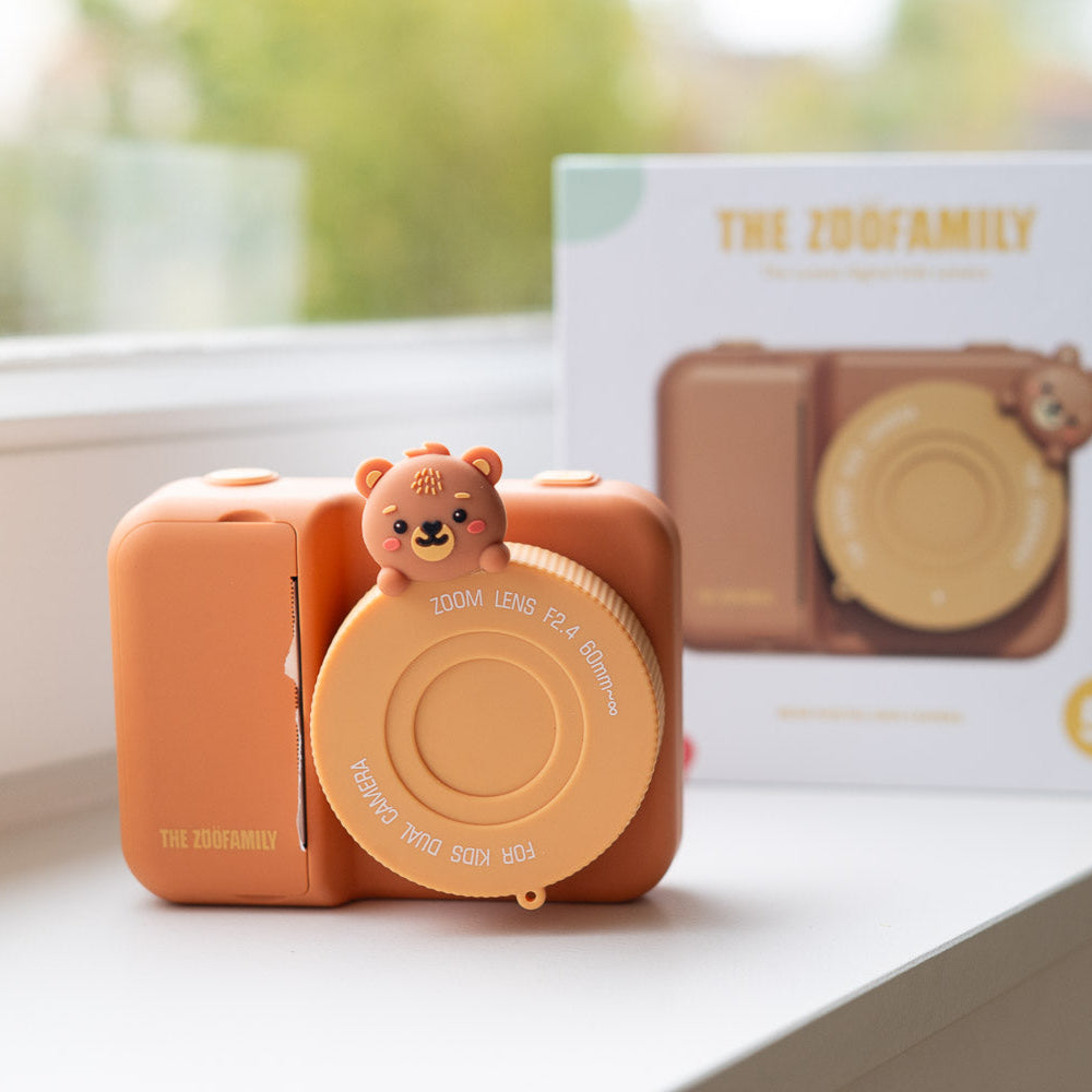 Cute camera with a bear on top, placed on a surface with a blurred background.