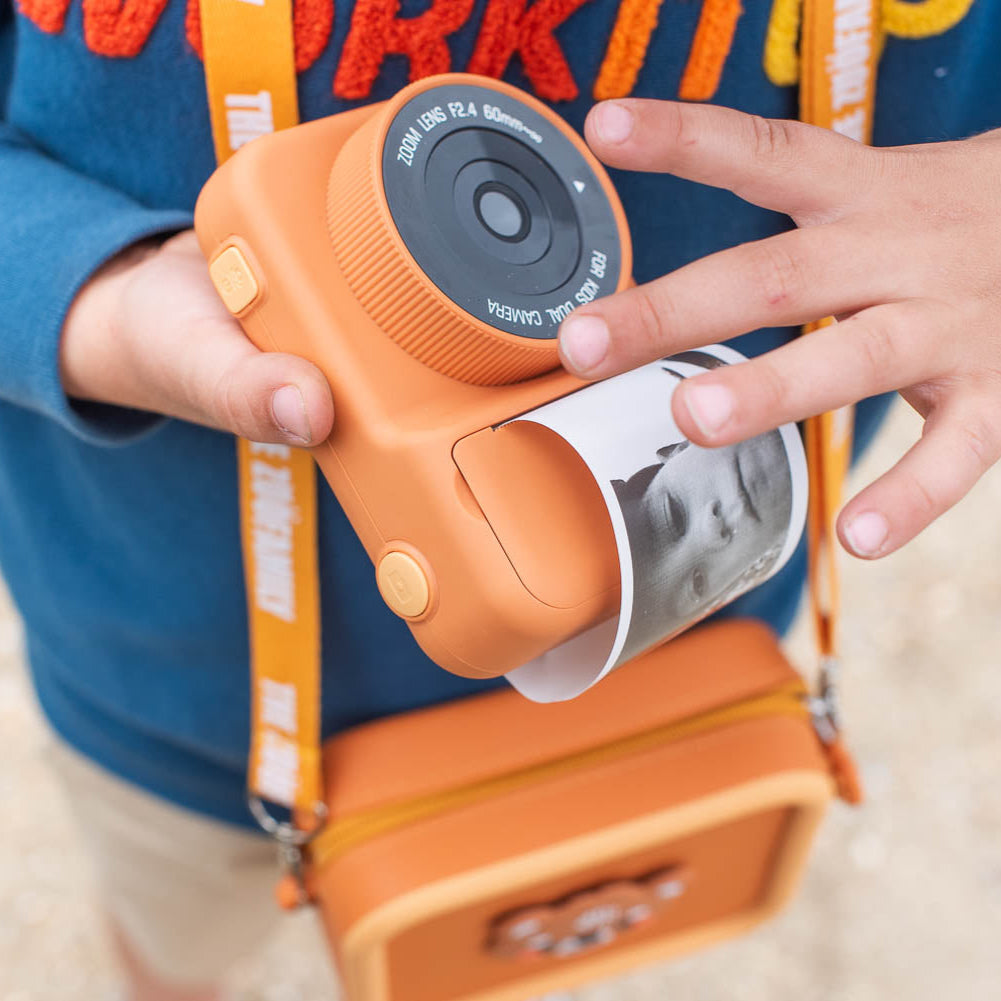 Child holding a toy camera with an orange and blue design, wearing a blue jacket with red text.