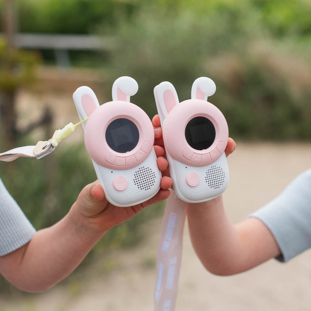 Two pink rabbit-shaped walkie-talkies held by two children outdoors.