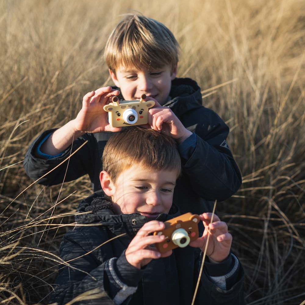 Two children playing with toy cameras in a field of tall grass.