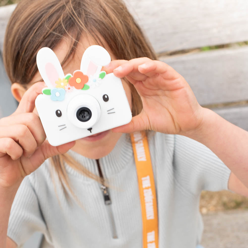 Child holding a white rabbit-shaped camera with a lanyard