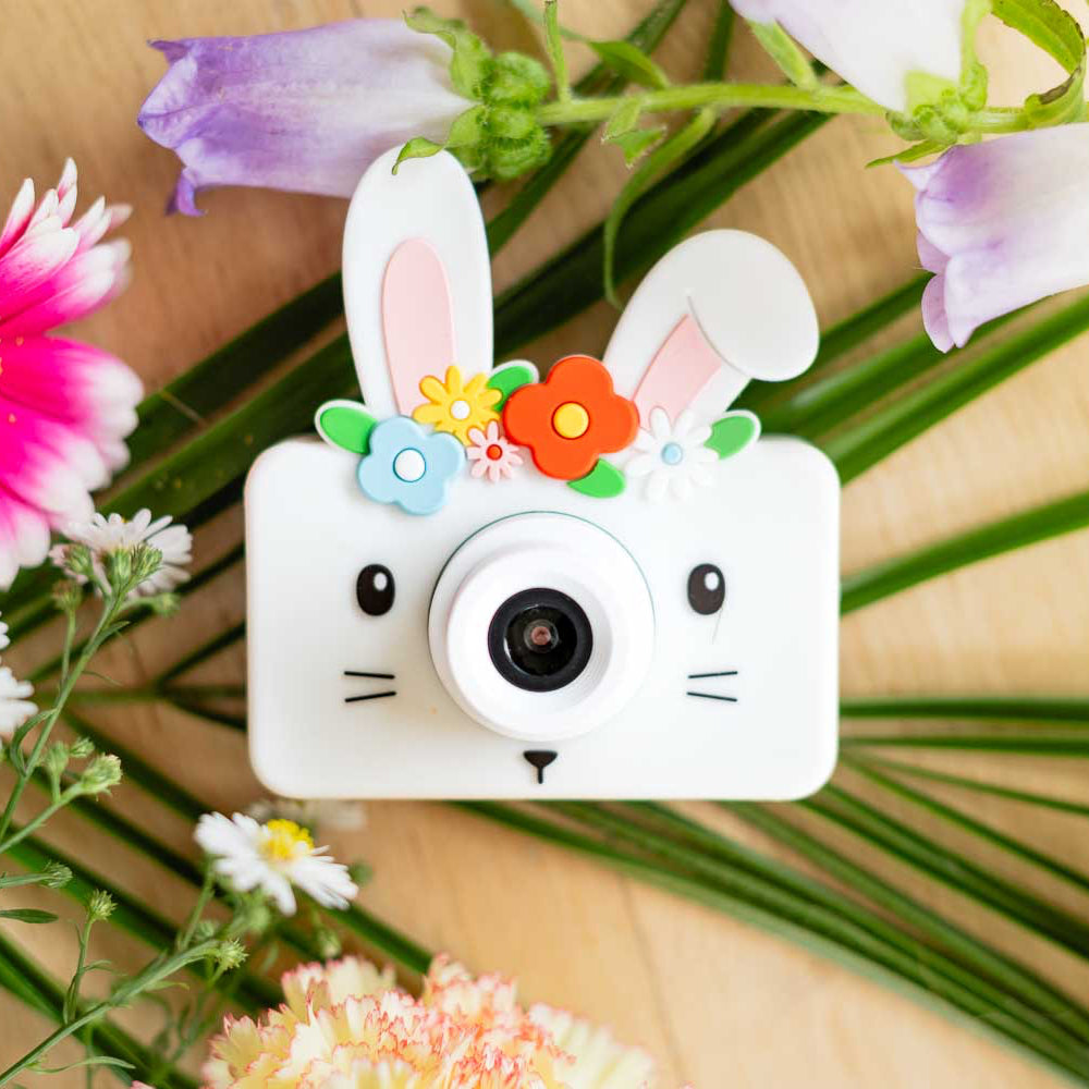 Camera with bunny design surrounded by flowers on a wooden surface
