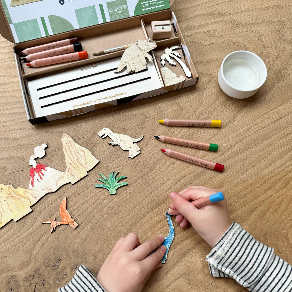 Children's craft kit with wooden dinosaur figures, markers, and a bowl on a wooden table.