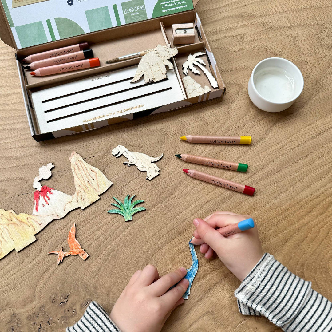 Children's craft kit with wooden dinosaur figures, markers, and a bowl on a wooden table.