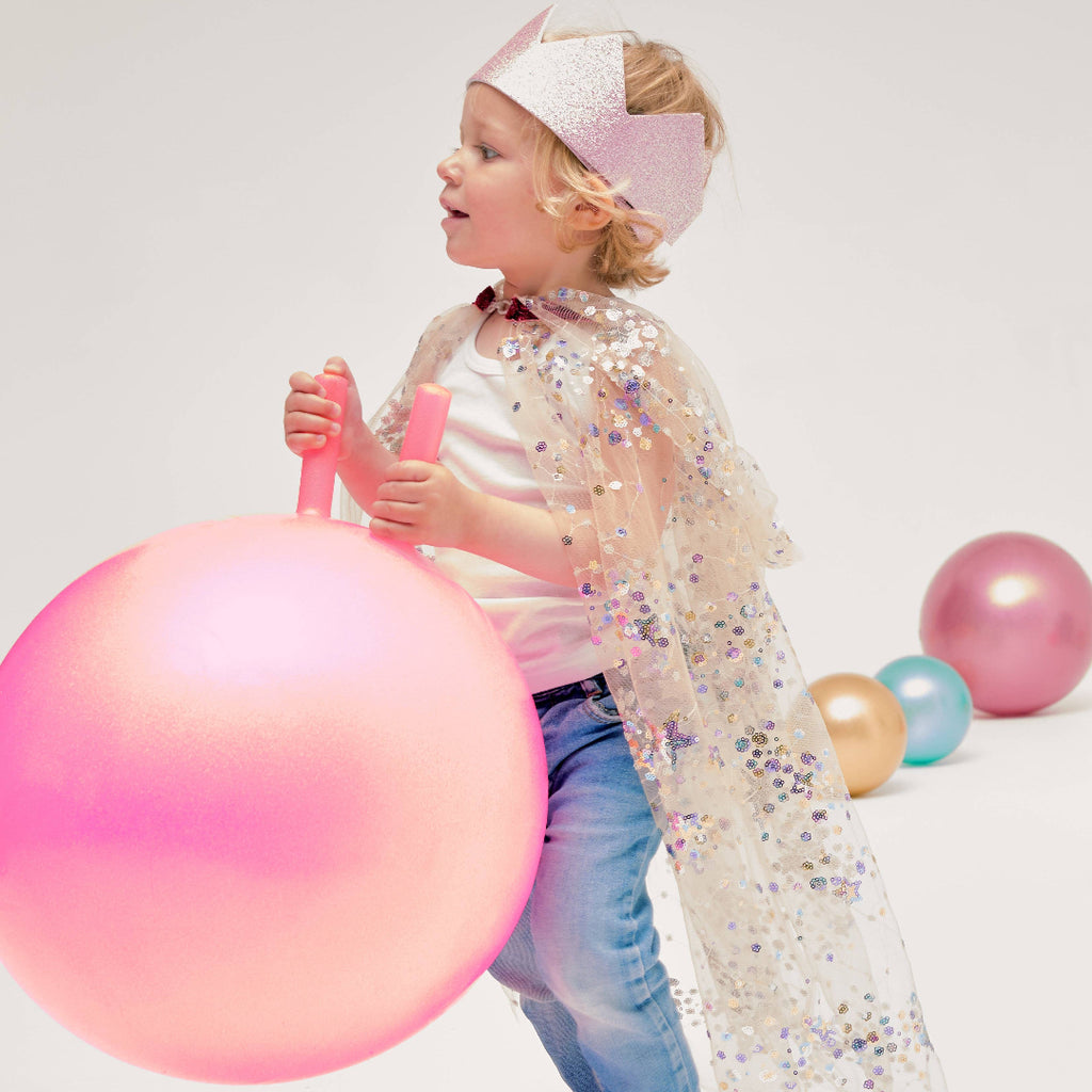 Child with a pink and purple ball and a sparkly cape on a white background
