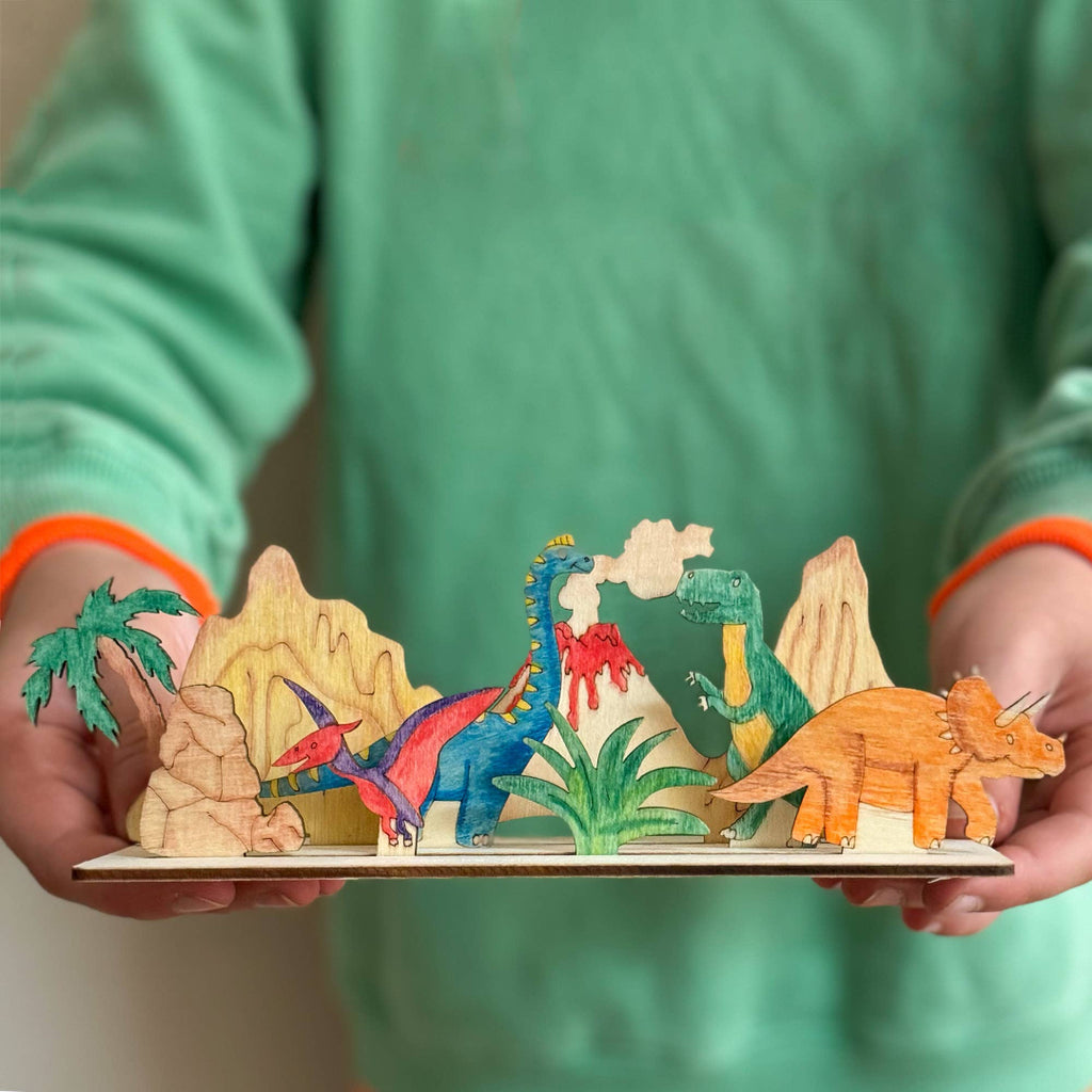 Colorful dinosaur model set held by a person wearing a green shirt with orange cuffs.