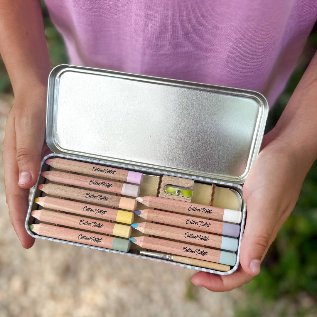 Person holding a set of colored pencils in a metal case with a blurred natural background