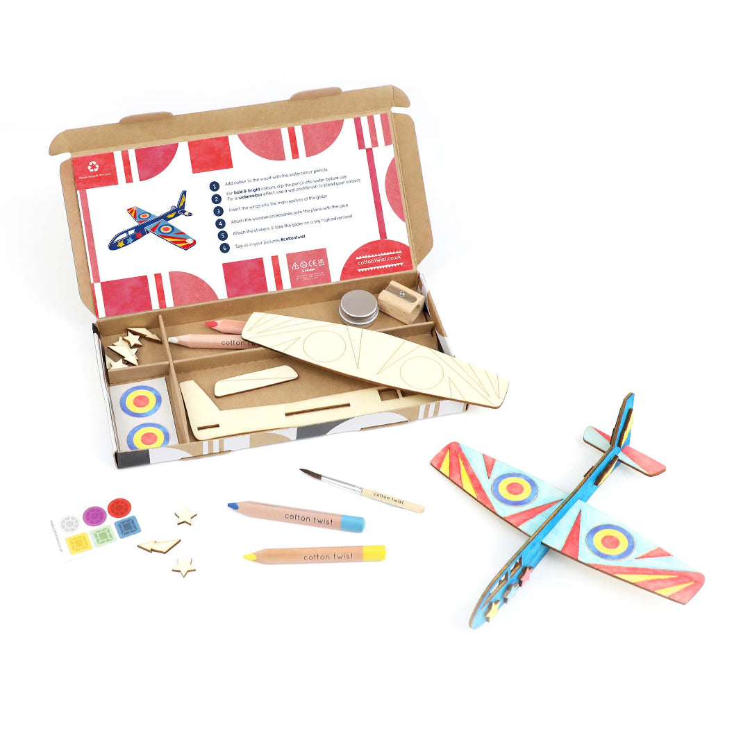 Children's craft kit with wooden airplane, paintbrushes, and other materials on a white background