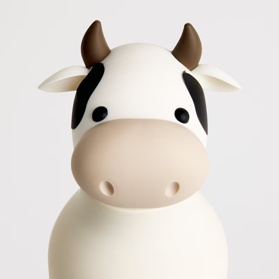 A cute cow-shaped container or figurine with a white body, black patches, and brown horns, photographed against a clean light gray background.