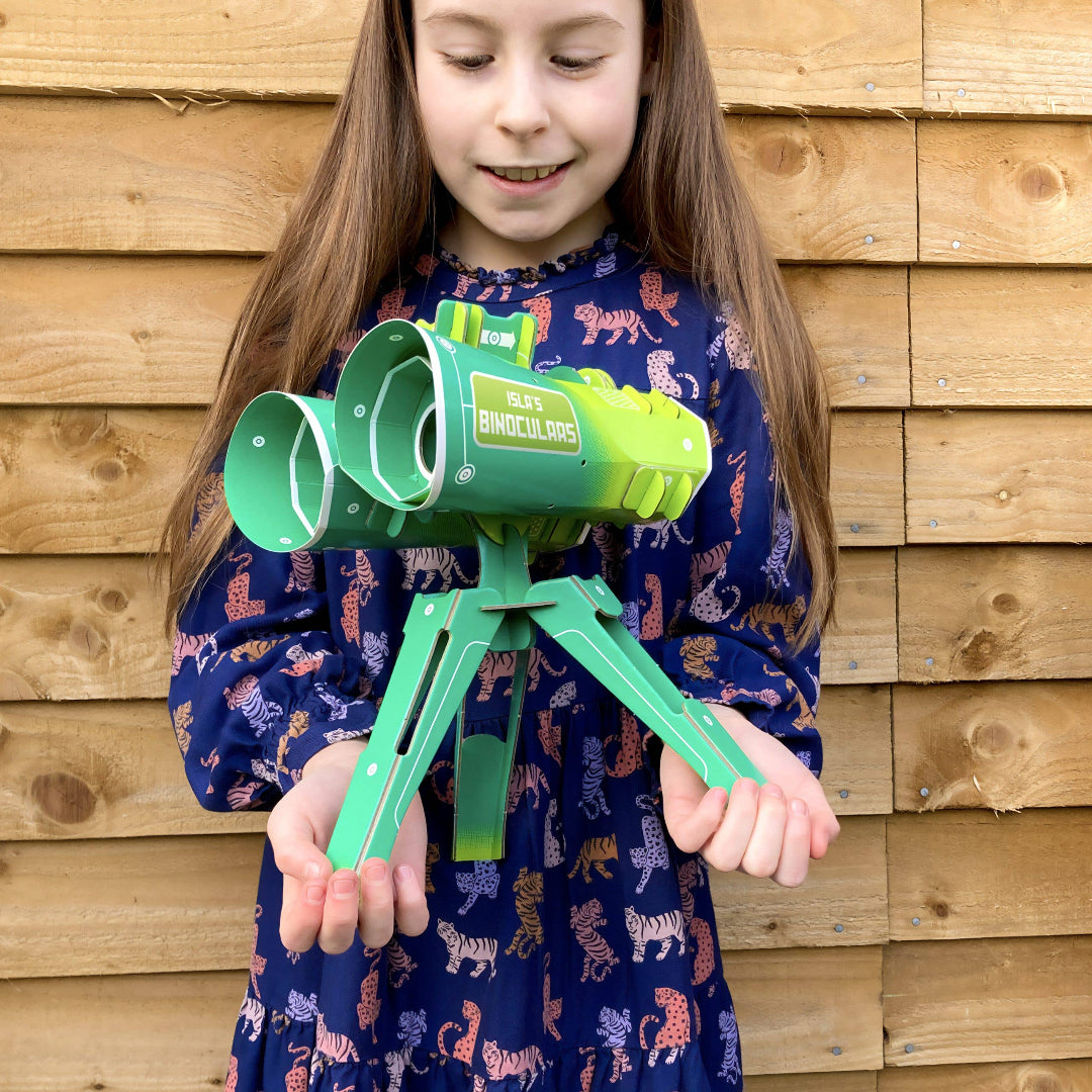 Child holding a green and white DIY biniculars against a wooden fence background