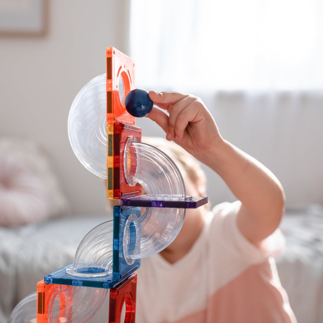 Child guiding a blue ball through a rainbow CONNETIX ball run with clear curved tubes