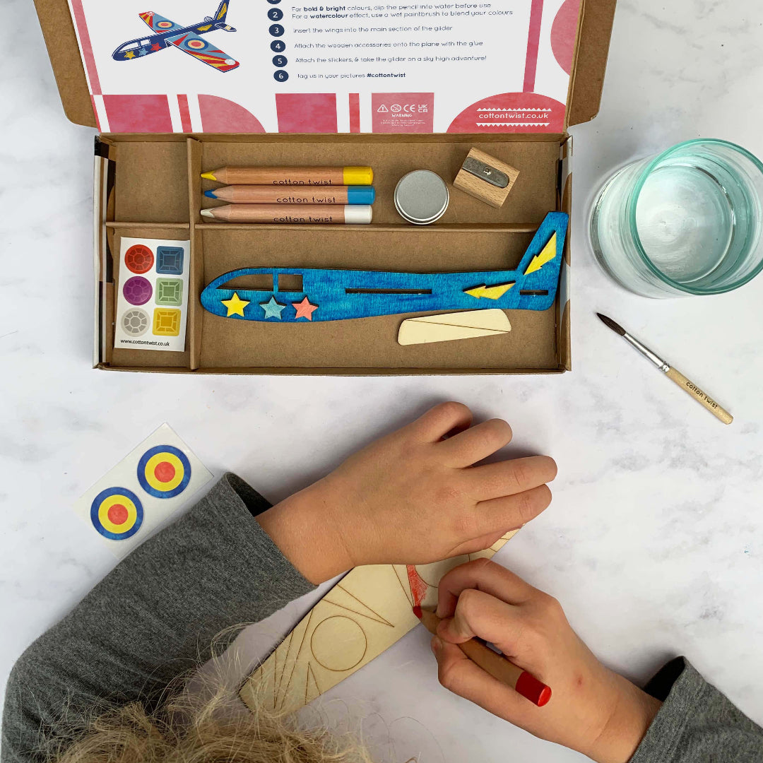 Children's craft kit with airplane model and art supplies on a marble surface