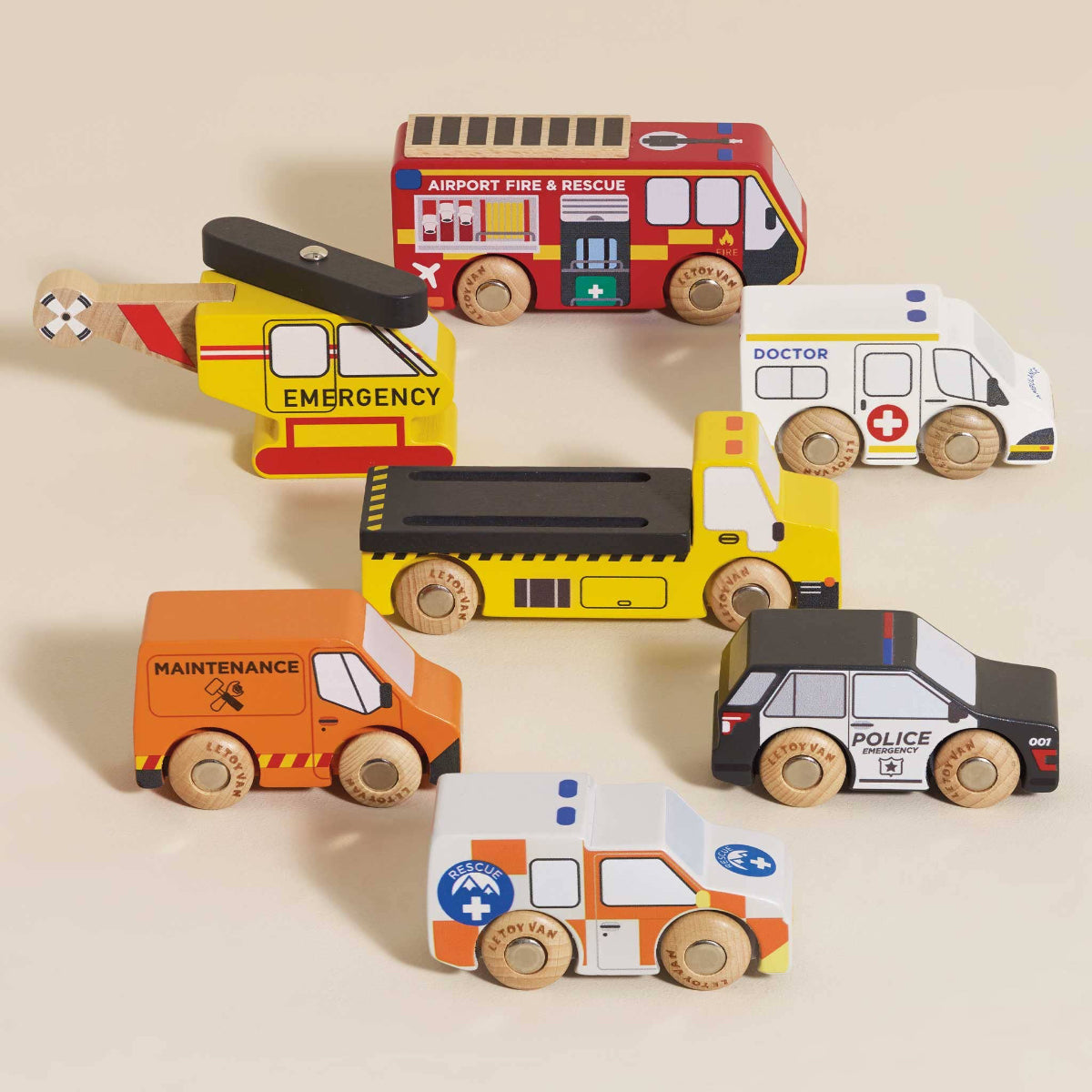 Set of colorful toy vehicles including a fire truck, ambulance, helicopter, and police car on a beige background.