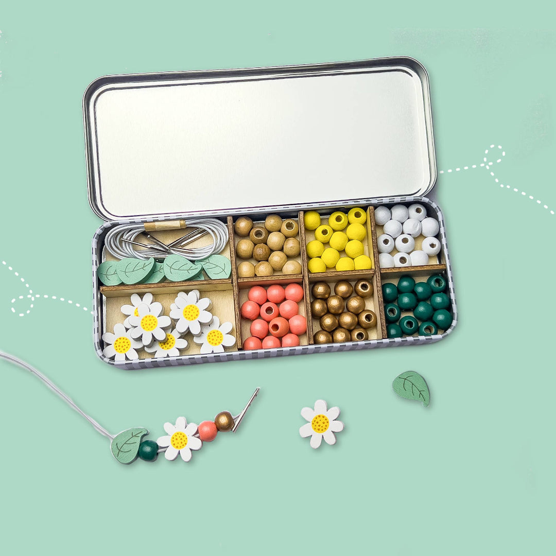 Jewelry-making kit with beads and tools in a tin on a light green background