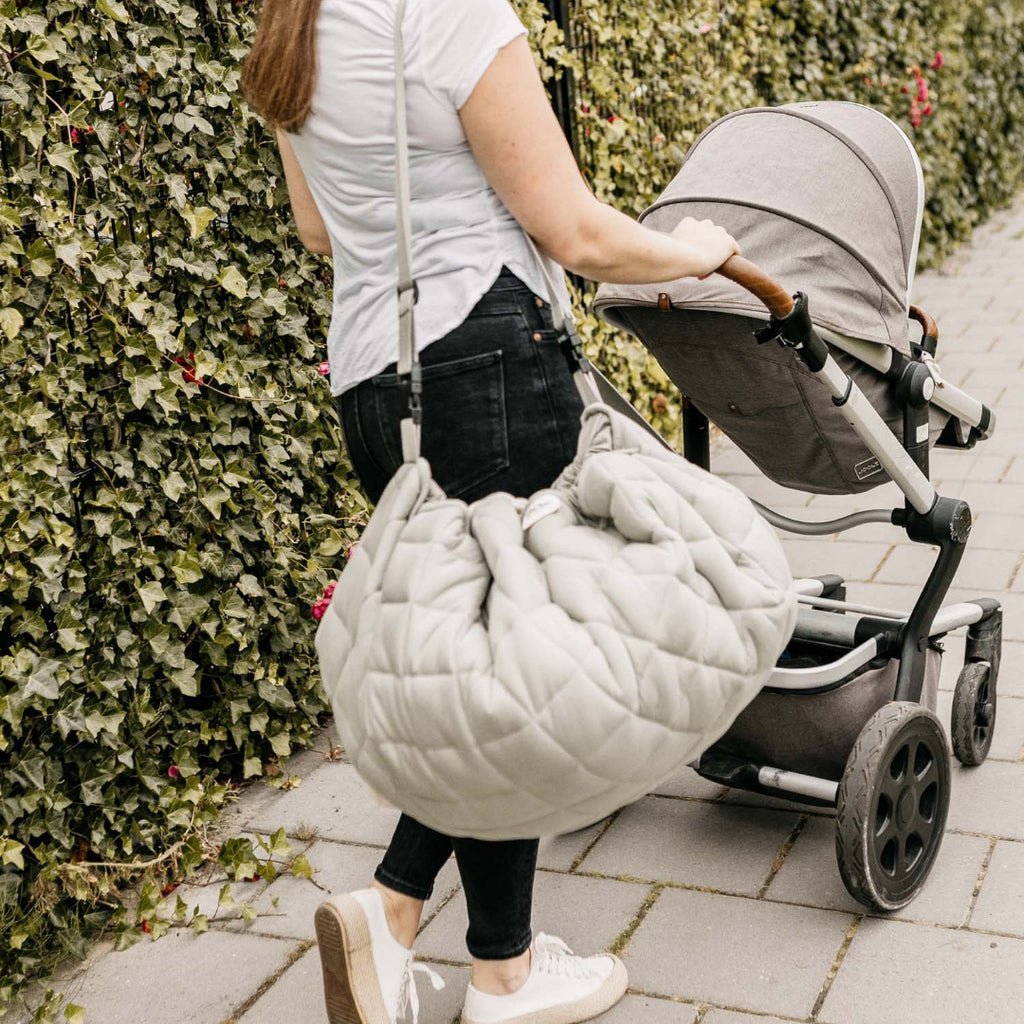 Woman pushing a stroller with a large bag on a sidewalk.