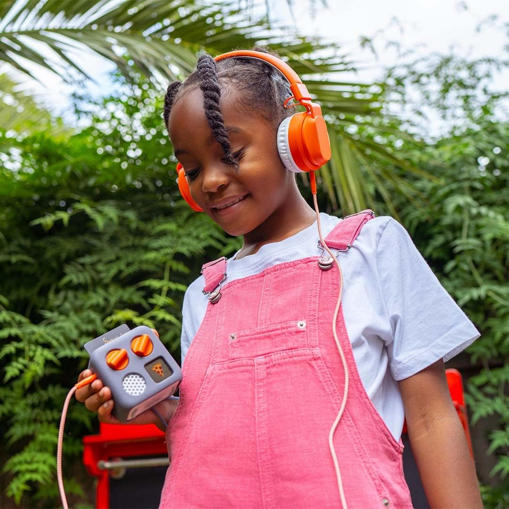 Child wearing orange headphones and holding a Yoto Mini outdoors