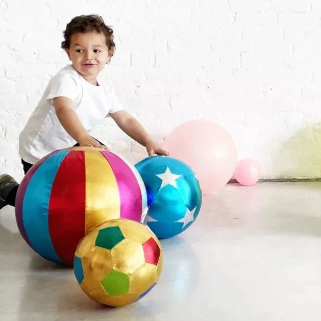 Child playing with colorful inflatable balls against a white brick wall.