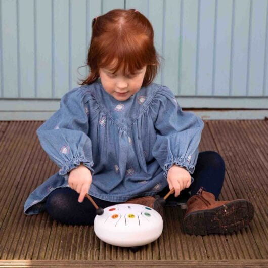 Child playing with a white musical instrument on a wooden floor.