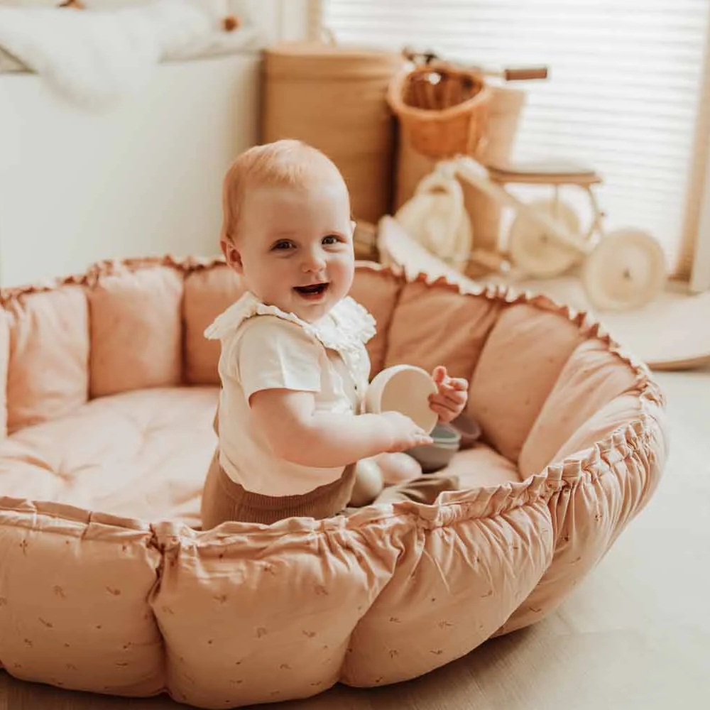 Baby sitting in a round, cushioned play mat cocoon  in a cozy living room.