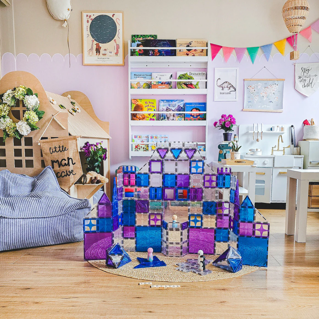 Colorful geometric blocks on a wooden floor with a child's play area in the background.